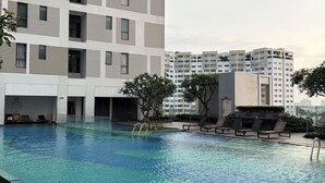 A swimming pool with a wooden deck, surrounded by a modern building with multiple balconies. - Rivergate-High Floor-Ben Thanh -Bui Vien (Ho Chi Minh City)