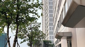 A pathway flanked by greenery and a modern building with a flat facade and large windows. - Rivergate-High Floor-Ben Thanh -Bui Vien (Ho Chi Minh City)