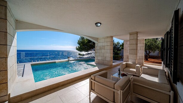 A pool with a view of the sea, outdoor seating, and a stone wall. - Villa Toma by Villas Guide (Orebic)