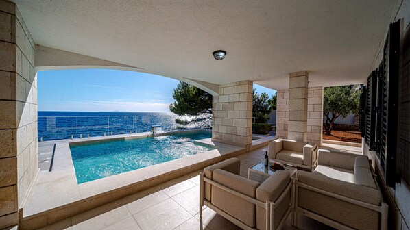 A pool with a view of the sea, outdoor seating, and a stone wall.