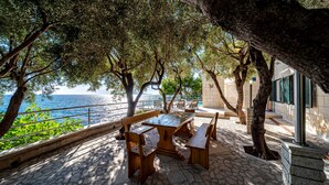 An outdoor seating area with stone flooring and wooden furniture, overlooking a body of water. - Villa Toma by Villas Guide (Orebic)