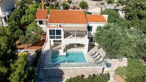 A multi-story house with a swimming pool, outdoor seating, and a stone facade.