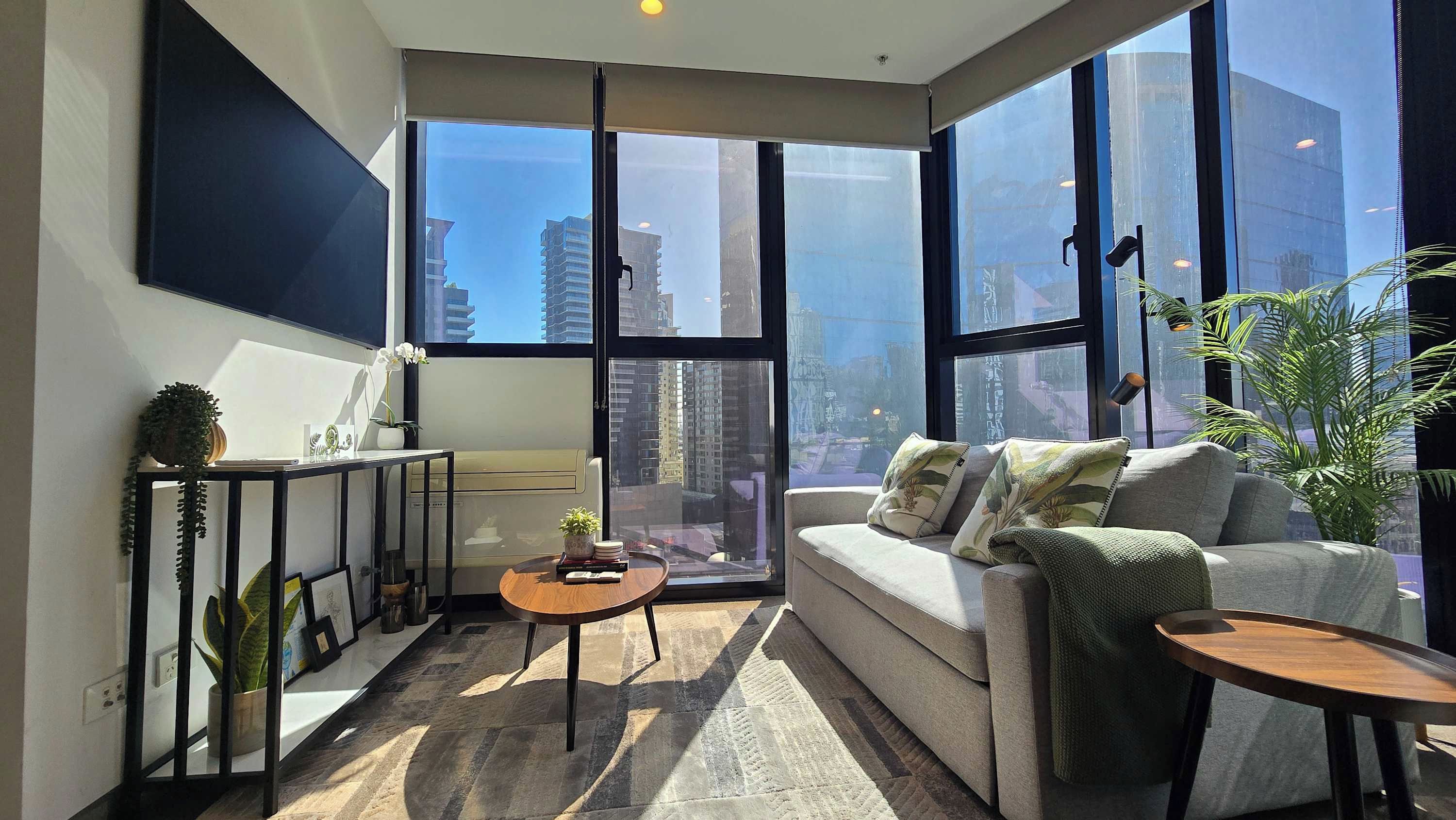 A modern living room with a sofa, coffee table, and large windows offering a city view.
