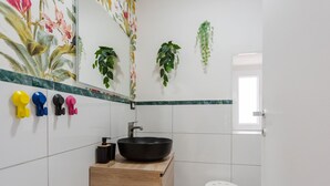 Un baño moderno con tocador de madera, un lavabo tipo cuenco negro y un inodoro blanco.