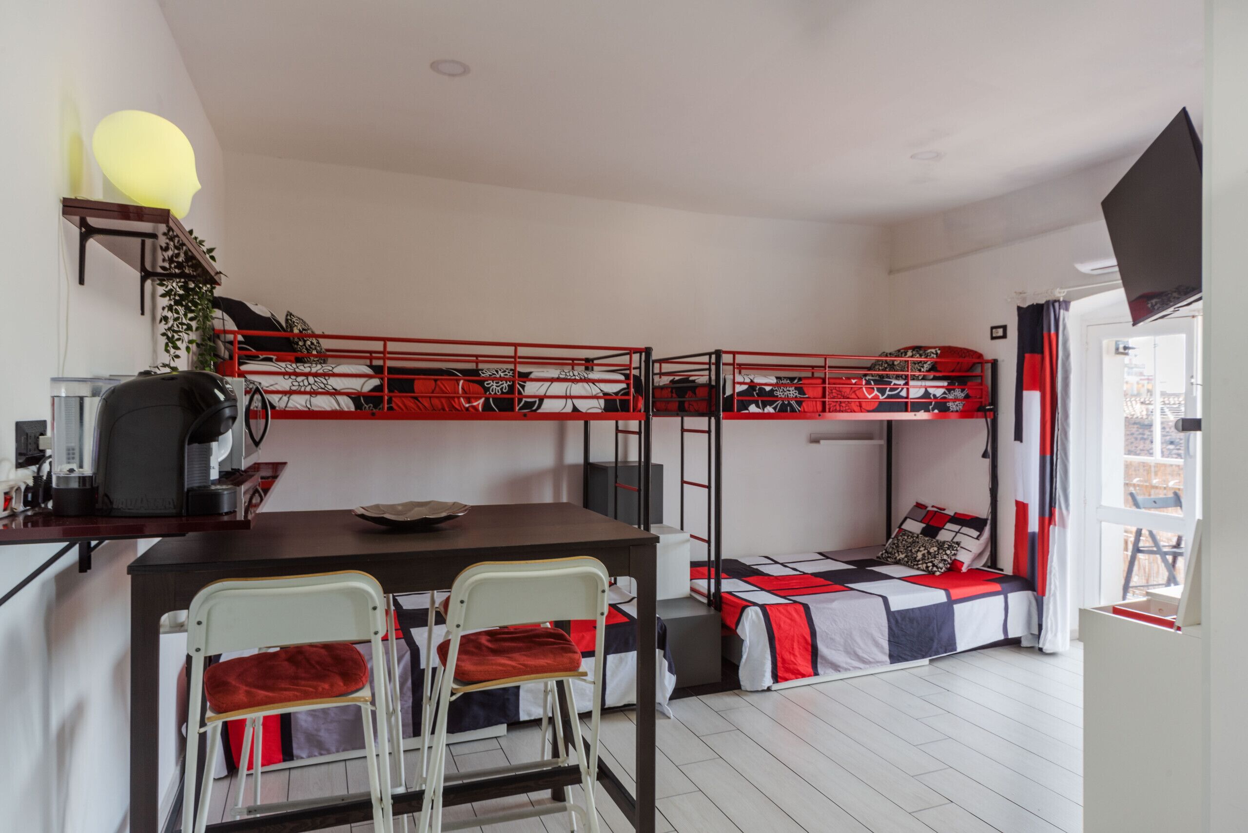 Un dormitorio con literas, un escritorio, sillas, una cafetera y un televisor.