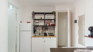 Una cocina compacta con armarios blancos, encimera de madera y pileta negra. Hay un estante pequeño sobre la pileta con diversos objetos.