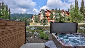 Un terrazzo in legno che conduce a una vasca idromassaggio con vista su un lodge e montagne boscose.