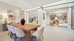 A modern dining area with a wooden table, white chairs, and a large vase. - GRAND MANOR HOUSE WIMBLEDON (London)