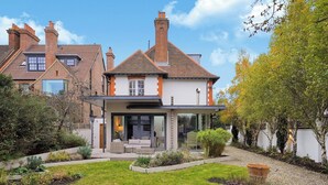 A modern house with a glass conservatory, a well-maintained garden, and a brick chimney. - GRAND MANOR HOUSE WIMBLEDON (London)