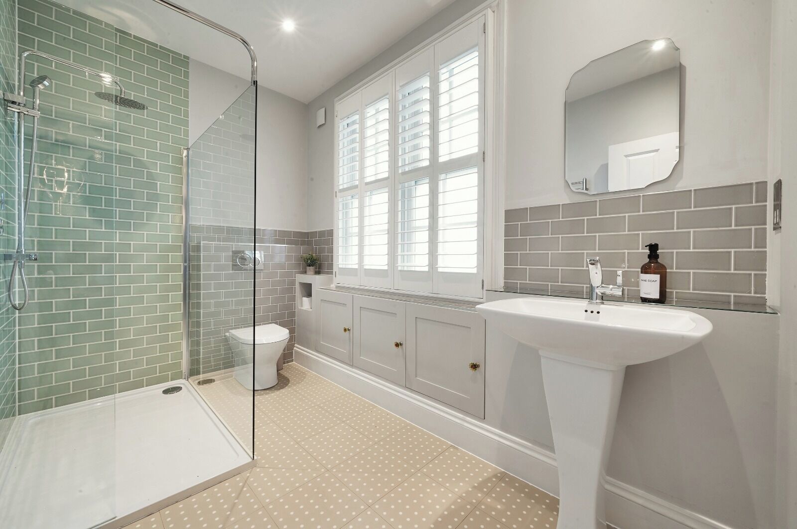 A bathroom with a glass-enclosed shower, a toilet, a sink, and a window with blinds.