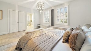 A bedroom with a large bed, a walk-in closet, and a bathroom visible through an open door. - GRAND MANOR HOUSE WIMBLEDON (London)
