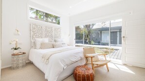 Een slaapkamer met een bed, een stoel, een klein tafeltje met een orchidee en een groot raam met uitzicht op het exterieur.
