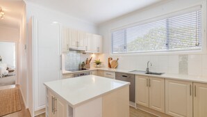 Een moderne keuken met witte kasten, een centraal eiland en een raam met zonwering.