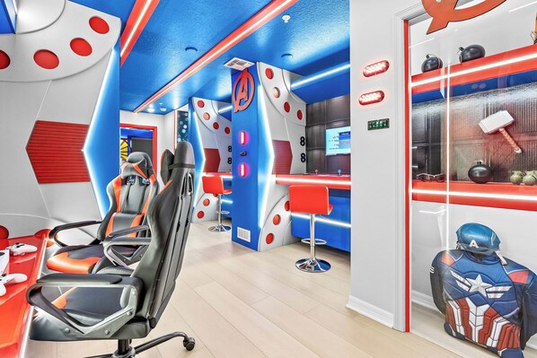 A modern gaming lounge with multiple gaming chairs, a bar area, and a Captain America statue. - Designer 5BR Gameloft Foam Pit Lazy River 16164 (Clermont)