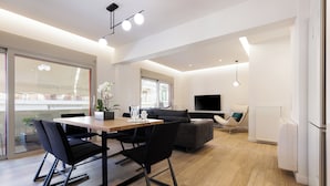 En moderne stue med spiseplads, en sofa, et fjernsyn og et stort vindue.