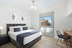Una camera da letto moderna con un letto grande, una scrivania e una sedia. Si vede una finestra con vista su un edificio.