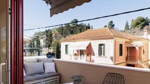 En balkon med sofa, et lille bord og en stol, med udsigt over en bygning med et tagdækket tag.