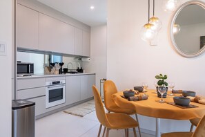 Eine moderne Küche mit weißen Schränken, einer Mikrowelle, einem Backofen und einem Essbereich mit einer gelben Tischdecke und Stühlen.