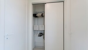 Ein weißer Kleiderschrank mit Regalen und Kleiderstange, einer Tür und einem Lichtschalter.
