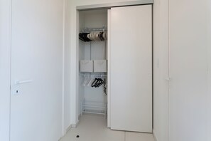 Ein weißer Kleiderschrank mit Regalen und Kleiderstange, einer Tür und einem Lichtschalter.