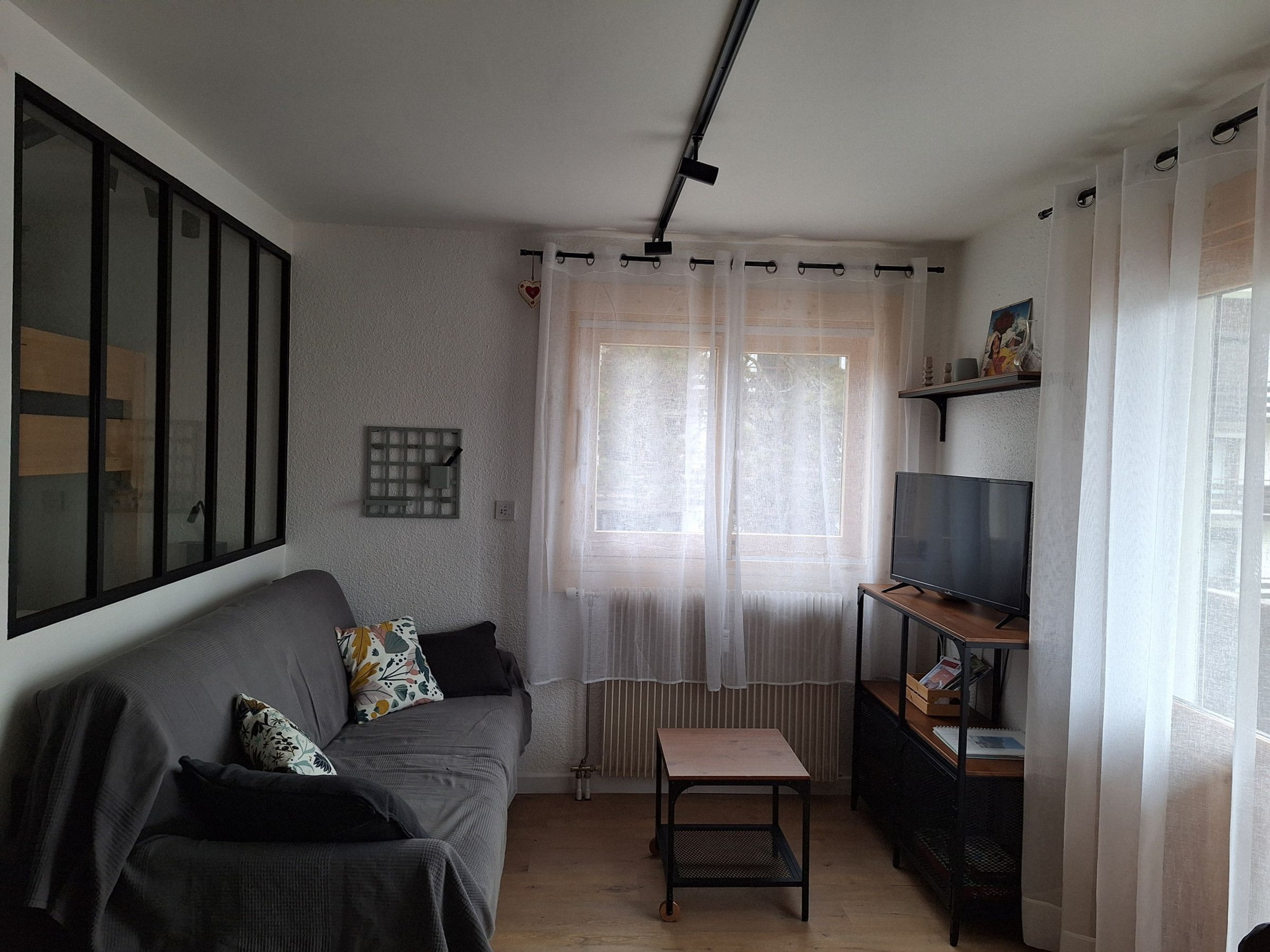 Ein Wohnzimmer mit grauem Sofa, einem kleinen Tisch, einem Fernseher und einer Heizung.
