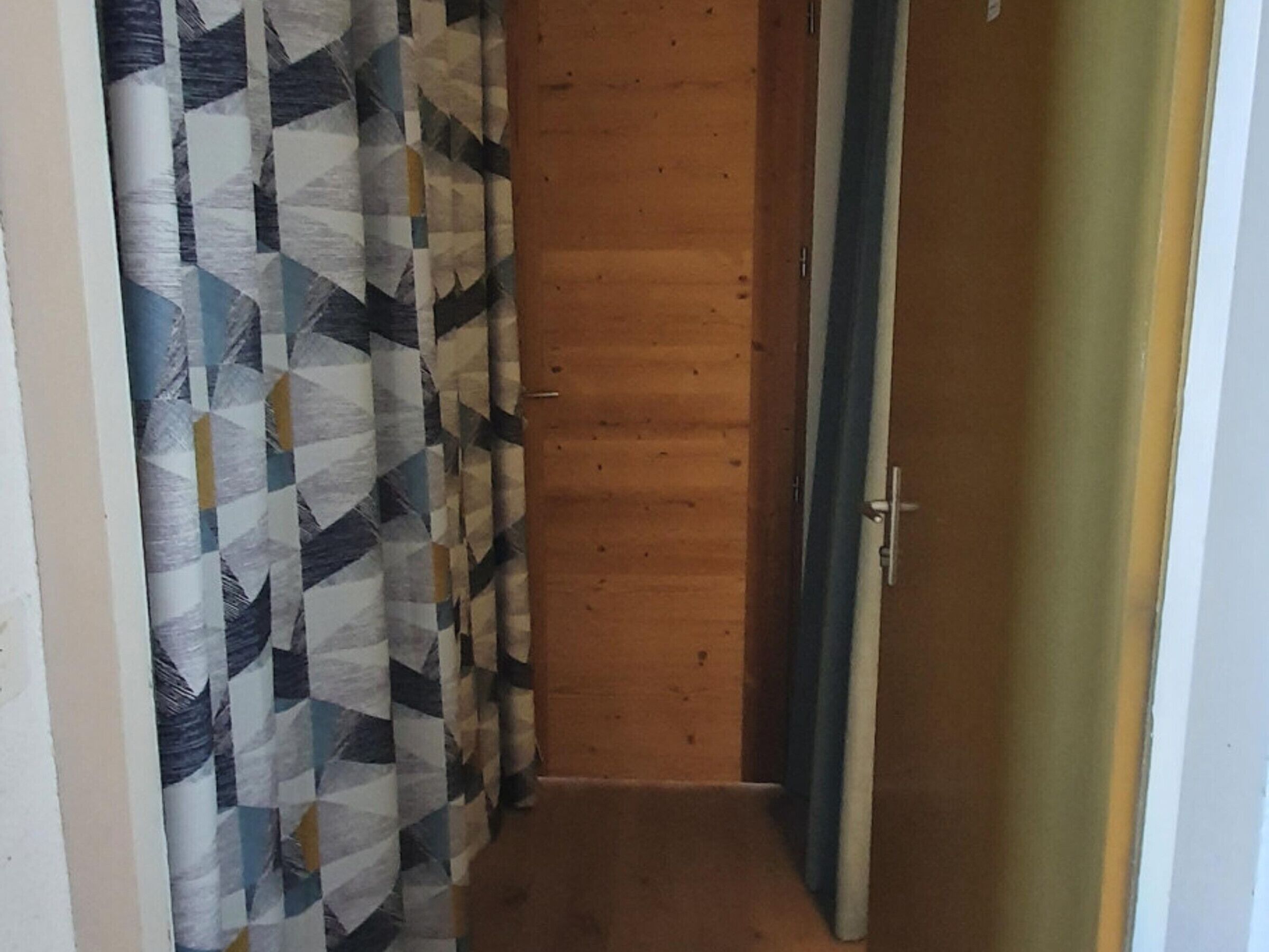 A narrow hallway with a wooden door on the right and a patterned curtain on the left.