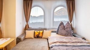 A bedroom with a bed, two windows, a view of a lake, and a table with a tablecloth. - Apartment "Paula" with Mountain View, Private Terrace and Wi-Fi (Leutasch)