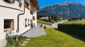 A white building with balconies, a paved area, and a mountain view. - Apartment "Paula" with Mountain View, Private Terrace and Wi-Fi (Leutasch)
