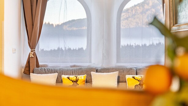 A room with a sofa, two arched windows, and a view of a lake and mountains. - Apartment "Paula" with Mountain View, Private Terrace and Wi-Fi (Leutasch)