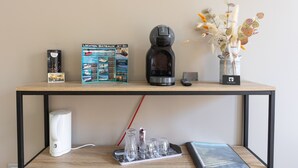 Una mesa de madera con una cafetera, un control remoto, un jarrón con plantas secas y un cuadro enmarcado.