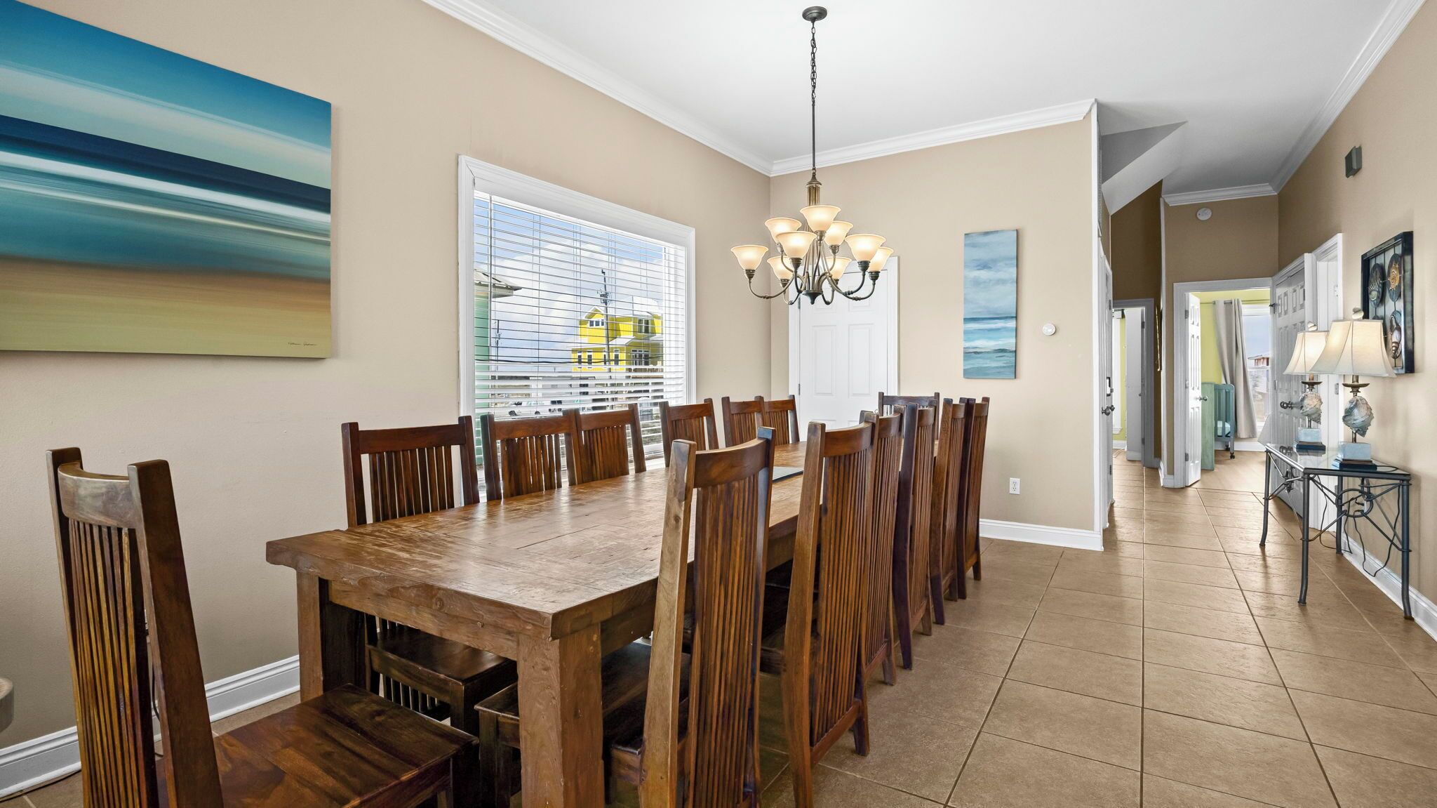 Un coin repas avec une table et des chaises en bois, un lustre et une vue sur un immeuble jaune par la fenêtre.