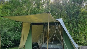 Una carpa con una combinación de colores verde y beige, una mesa y una silla instalados al aire libre.