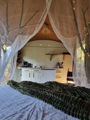 Une chambre confortable avec un lit à baldaquin, une kitchenette dotée de meubles blancs et une vue sur l’extérieur.