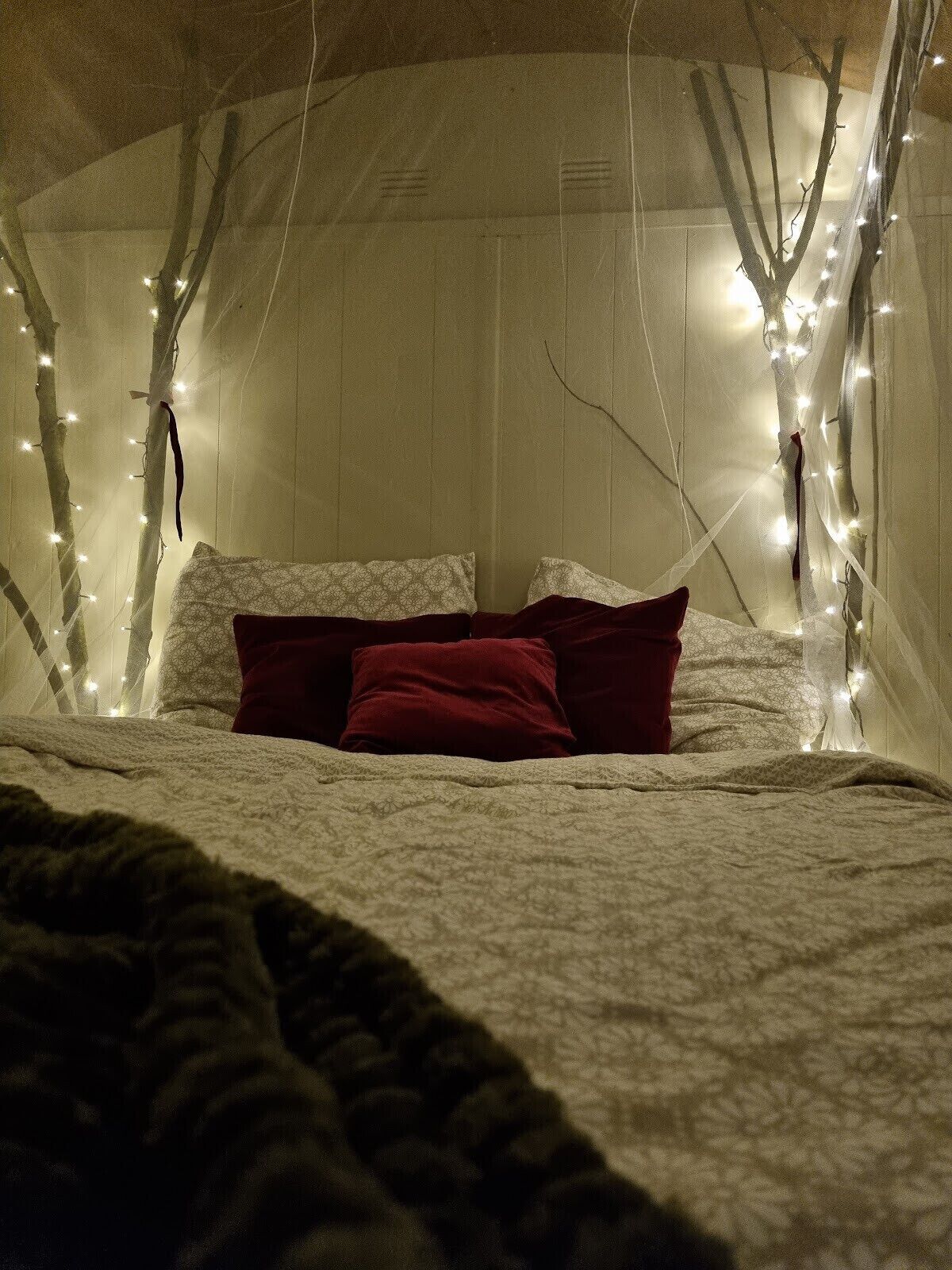 Une chambre confortable avec un lit, des oreillers et des guirlandes lumineuses créant une atmosphère chaleureuse.