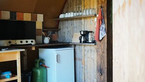A rustic kitchen with a wood stove, a coffee maker, and a small refrigerator.