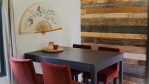 Un comedor con una mesa de madera y sillas rojas, un abanico decorativo y una pared de madera rústica.
