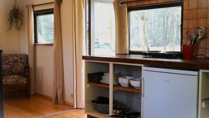 Una cocina compacta con refrigerador, estantes con vajilla y un ventanal con cortinas.