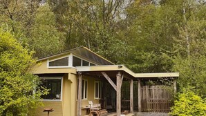 A single-story house with a covered porch, a small deck, and a fenced backyard. - Camping Ont Moeten - Hallertau (Rekken)