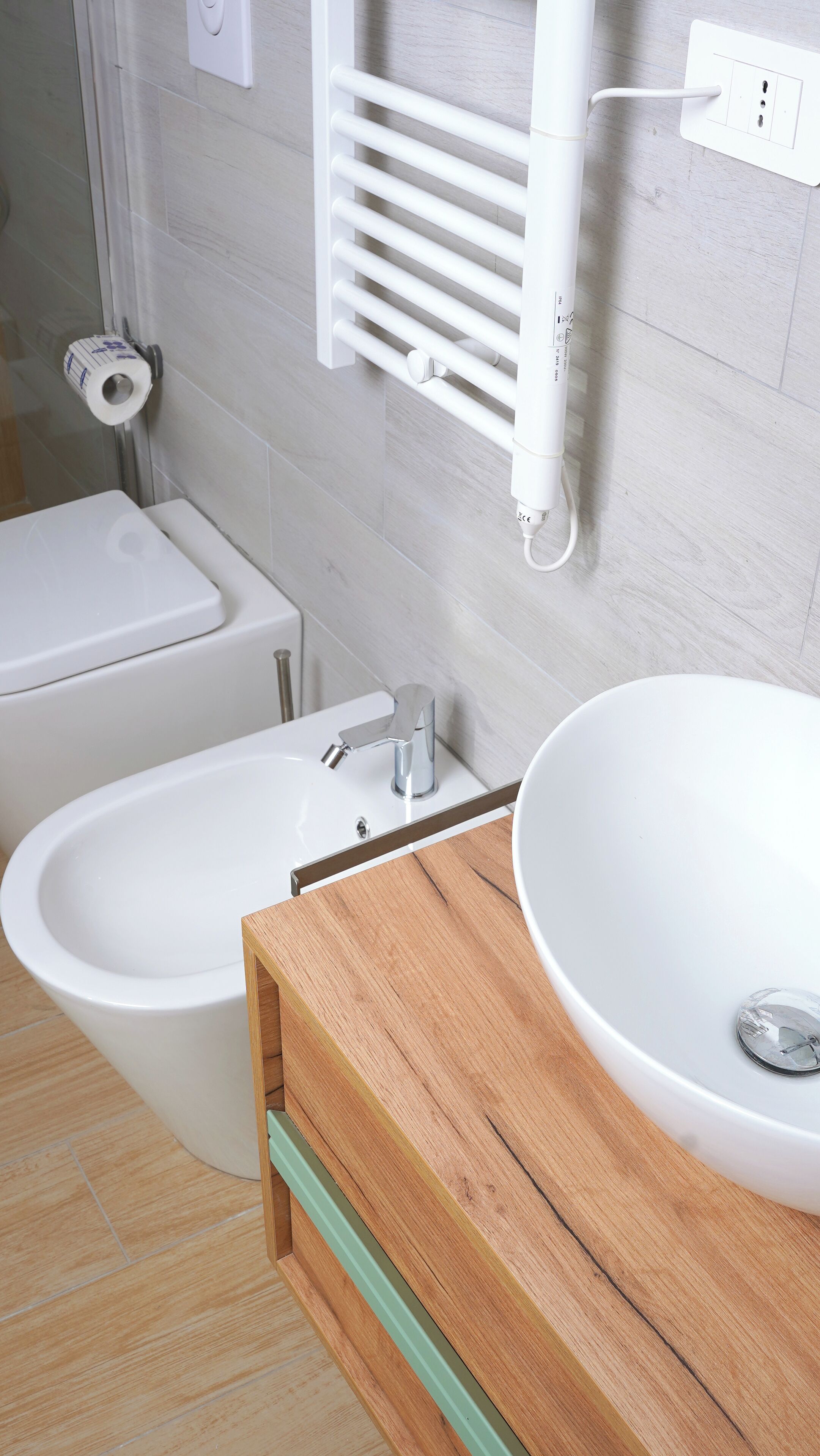 A bathroom with a toilet, bidet, and sink with a wooden vanity.