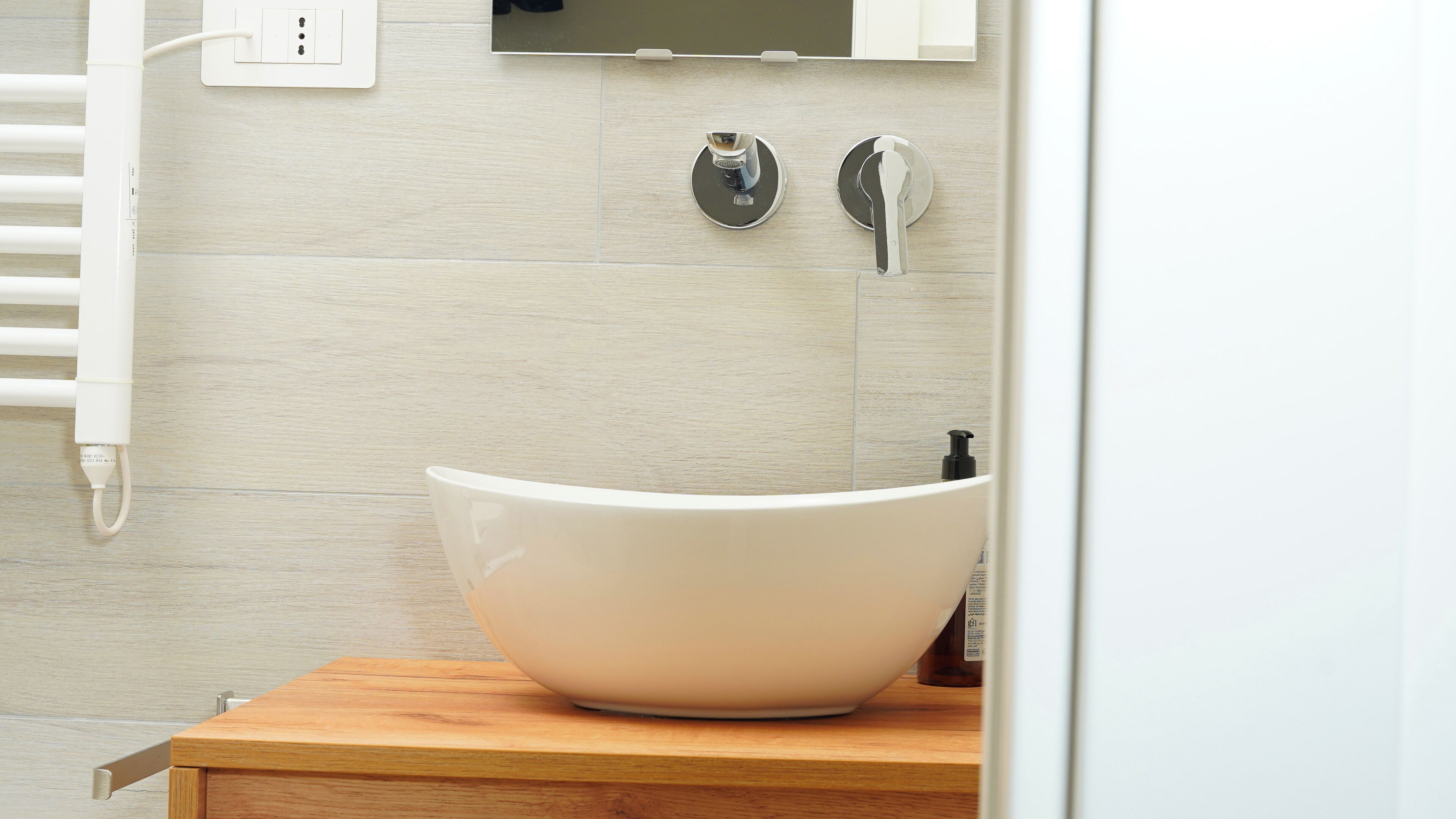 Une salle de bain moderne avec un lavabo sur colonne blanc, un meuble-lavabo en bois, un porte-serviettes et un miroir fixé au mur.