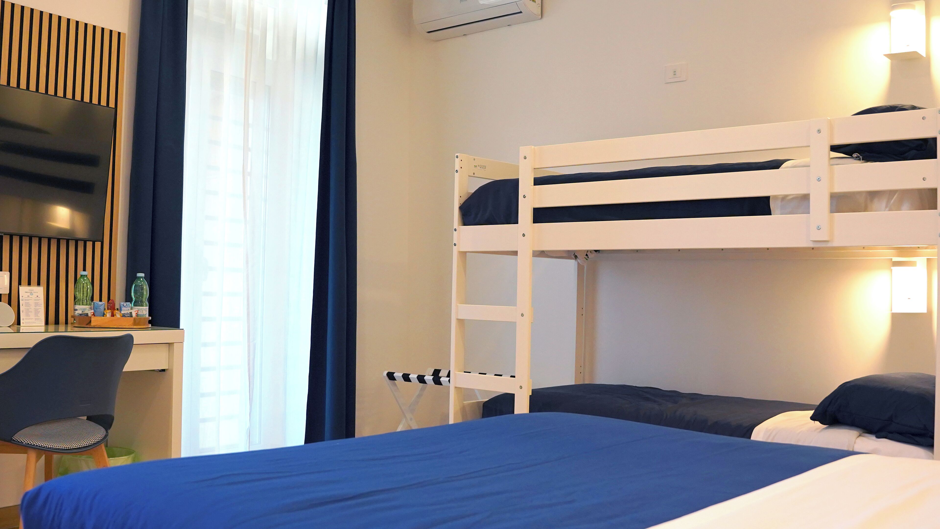 Habitación con literas, un escritorio, una silla, un televisor y una ventana con cortinas.