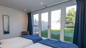 Ett sovrum med två sängar, en stol, ett stort fönster och utsikt över en trädgård på baksidan av huset.