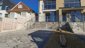 En modern tvåvåningsbyggnad med ett trästaket, en asfalterad uppfart och ett område med grus.