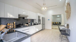 A modern kitchen with white cabinets, a stainless steel range hood, and a black countertop. There is a dining area with a black metal chair and a table. - Villa Haut Standing - 4 Suites - Heated Pool 20 minutes from Marrakech (Rha)