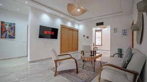 A modern living room with a flat-screen TV, a sofa, a chair, a coffee table, and a decorative wall hanging. - Villa Haut Standing - 4 Suites - Heated Pool 20 minutes from Marrakech (Rha)