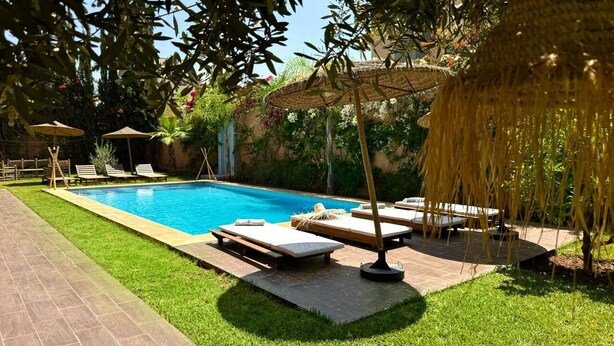 A swimming pool with lounge chairs and umbrellas, surrounded by greenery and a brick pathway. - Villa Haut Standing - 4 Suites - Heated Pool 20 minutes from Marrakech (Rha)