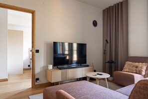 Ein stilvolles Wohnzimmer mit Flachbildfernseher, einer Couch, einem Couchtisch und einer Lampe.