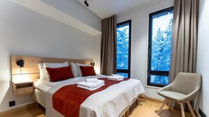 Een moderne hotelkamer met een groot bed, een nachtkastje, een stoel en twee ramen met uitzicht op sneeuw.