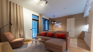 Een moderne woonkamer met een bank, fauteuil en salontafel. Er is een keuken met kasten en een raam.