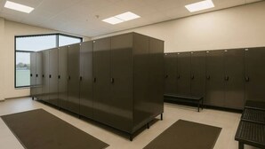 Een kleedruimte met metalen kasten, een bank en een groot raam dat voor natuurlijk licht zorgt.